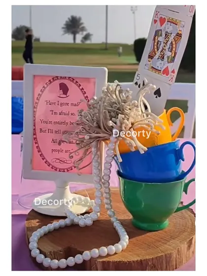 A creative centerpiece with stacked teacups, playing cards, and a framed quote from Alice in Wonderland.