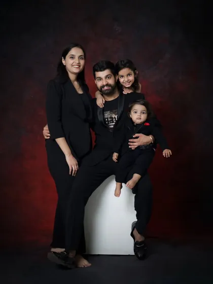 A beautiful family of four, all dressed in black, against a rich, textured backdrop. This classic studio portrait is elegant and will be a cherished family heirloom.
