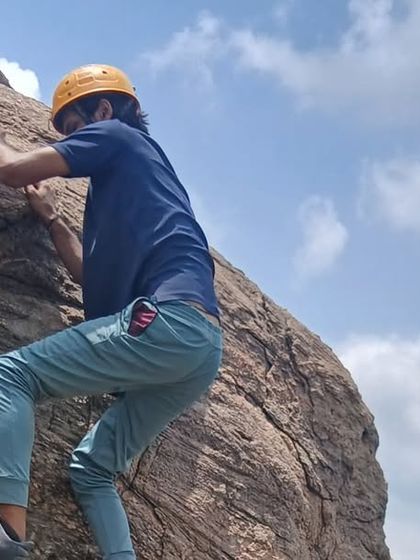 A close-up of a young climber focusing on his hand and foot placement on the textured rock surface of Ramanagara.