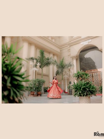 A wide shot showing the bride-to-be twirling in her vibrant lehenga in a grand courtyard. This image captures the joy and energy of the moment against a beautiful architectural backdrop.