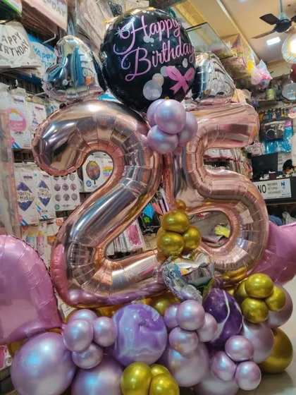 A grand bouquet for a 25th birthday celebration. This arrangement features large rose gold number balloons, a printed 'Happy Birthday' foil, and a base of purple, pink, and gold chrome balloons.