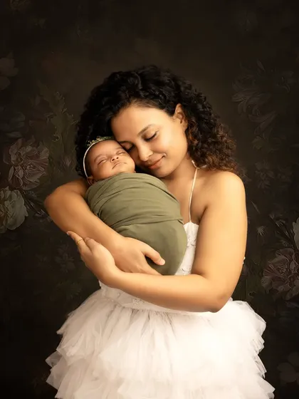 A tender mother and child portrait. The mom holds her newborn baby close, creating a beautiful and emotional image against a classic, dark floral background.