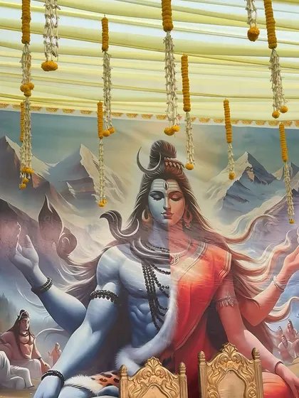 A unique backdrop featuring a depiction of Ardhanarishvara (Shiva and Parvati) for a spiritual or wedding related event. The setup is adorned with hanging marigold strings, blending divine art with traditional decor.