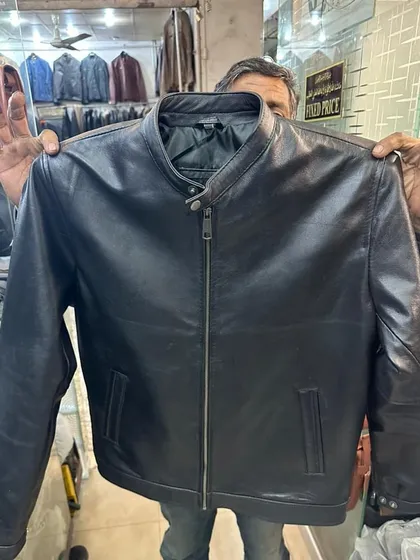 Holding up a classic black leather jacket to show its full design. This style is a staple and the quality from my Karachi source is 'mmg elok'.