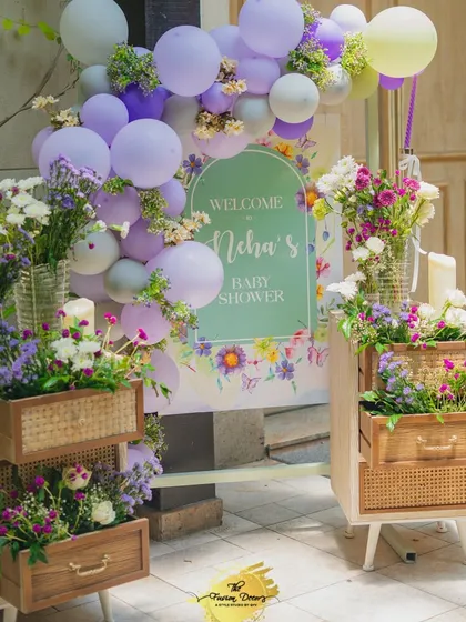 Welcome your guests in style. ✨ I love creating personalized entryways like this one, featuring a custom welcome sign for 'Neha's Baby Shower' framed by cascading balloons and unique floral arrangements spilling from rustic wooden drawers.