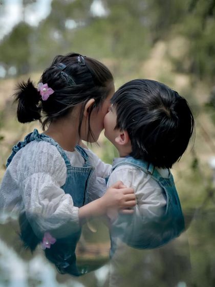 An artistic and intimate shot of two siblings sharing a kiss, with their reflection captured in the foreground.