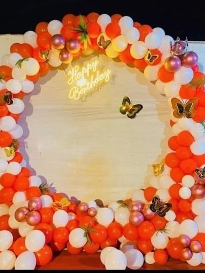 An orange and white balloon ring with butterfly accents and a neon sign.