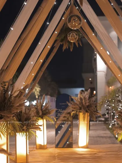 A bohemian-glam themed entrance featuring a canopy of white and beige drapes, pampas grass arrangements, and disco balls. This creative design is perfect for a relaxed yet stylish corporate party or team celebration.