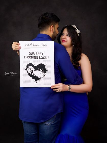 A creative pregnancy announcement photo. The couple shares a loving glance while holding a custom "Newborn Times" poster, making for a memorable and fun maternity shoot.