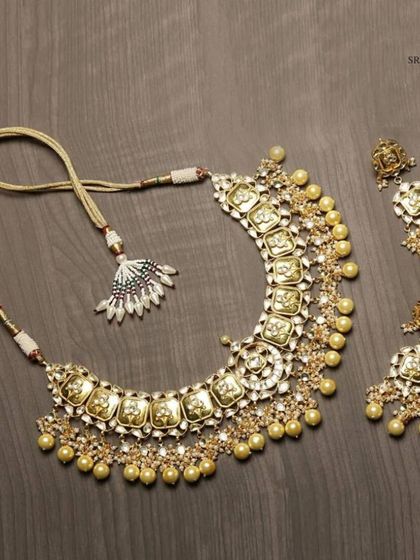 A classic Kundan necklace set with a antique gold finish and pearl droplets. This timeless piece is perfect for pairing with a silk saree or a traditional lehenga.