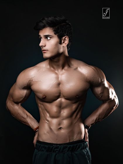 A confident three-quarter turn pose with hands on hips. The lighting is designed to highlight the chest, shoulders, and the vascularity in the arms, presenting a complete and powerful upper body look.