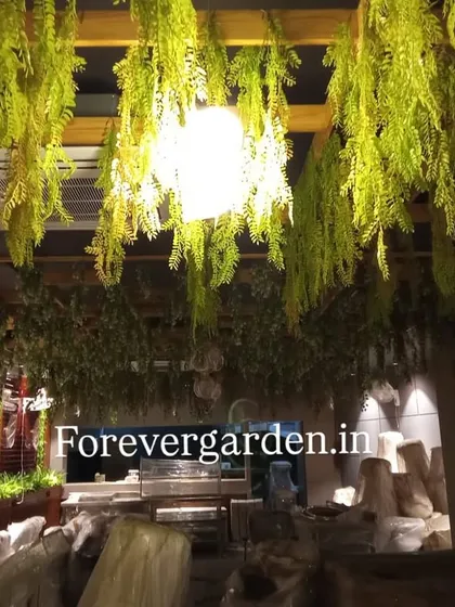 The same ceiling installation illuminated by a warm light, showcasing the vibrant green tones of the artificial foliage.
