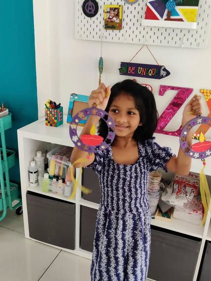 A young girl holding up the two lovely Diwali hangings she made, ready to decorate her home.