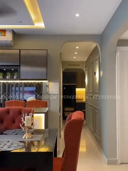 A glimpse into a luxurious dining area with plush, high-back red chairs. The corridor features elegant wall moulding and sconce lighting, leading the eye through the space and highlighting the rich material palette.