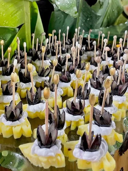 Pineapple pieces topped with cream and black olives, arranged in a flower-like pattern. This is another example of the creative and artistic fruit preparations I offer.