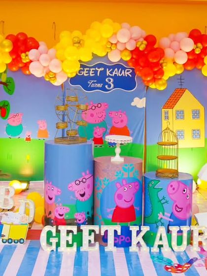 A cheerful Peppa Pig-themed third birthday party. This setup includes a full-scene backdrop of Peppa's world, character-printed plinths, and a bright, colorful balloon arch.