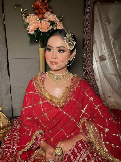 A bride seated in a classic red suit-style lehenga, showing the intricate gold grid pattern.