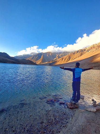 A trekker enjoying the stunning view of the crystal-clear Chandratal Lake on our Hampta Pass trek.