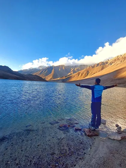 A trekker enjoying the stunning view of the crystal-clear Chandratal Lake on our Hampta Pass trek.