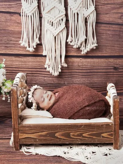 A baby sleeping on a dark wood bed against a wooden backdrop, accented with a macrame wall hanging and soft lamp light for a cozy, rustic feel.