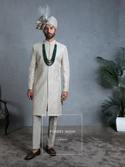 A view of the ivory sherwani without the stole, highlighting the intricate artistry on the garment itself. Paired with an emerald mala, it’s a look of quiet strength.