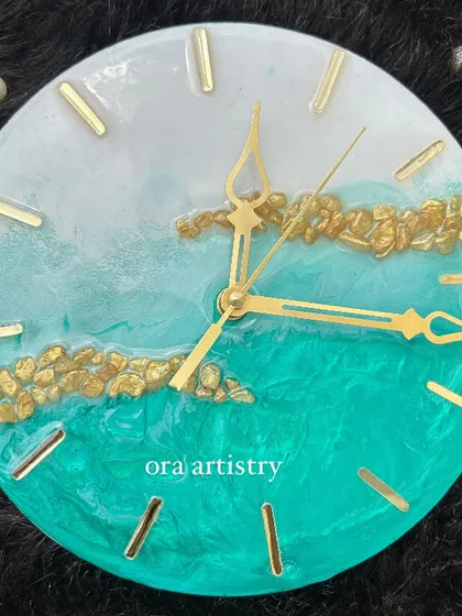 A mini resin clock with a soft teal and white design, accented with a band of gold stones.