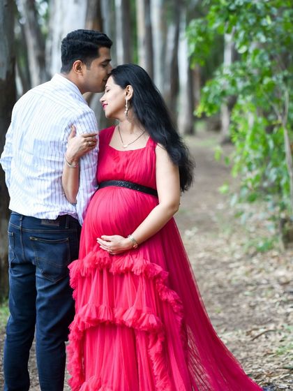 A romantic portrait of a couple in the woods. The dad-to-be kisses his partner's forehead as she holds her bump.