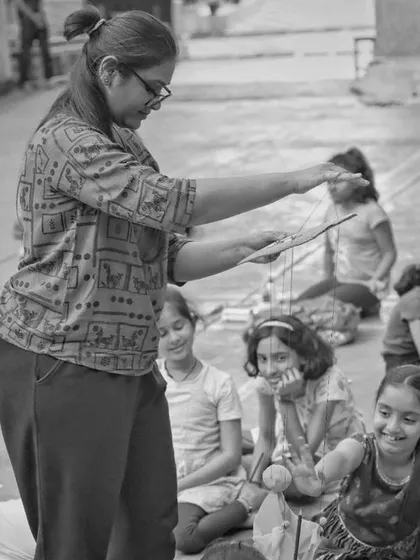 A black and white shot of me teaching a group of girls how to use a basic string puppet. There's so much joy in seeing them learn a new skill and succeed.