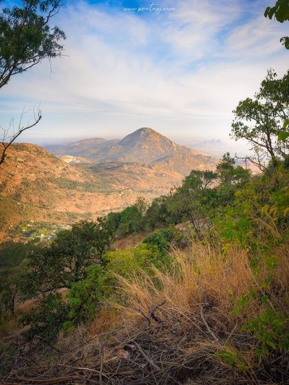 A view of Skandagiri hill from my archives. The photo is framed by trees, looking out over the dry landscape towards the popular trekking destination near Bangalore.