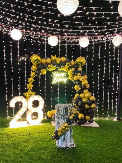 I transformed this outdoor garden space for a 28th birthday party. The decoration is defined by a canopy of fairy lights, a black and gold balloon arch, a neon sign, and large marquee numbers.
