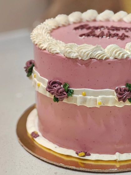 A close-up of the side of the pink vintage cake, showing the detailed ribbon of frosting and small floral accents.