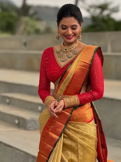 I love creating striking contrasts. Here, a custom red net blouse with full-length embroidered sleeves brings a bold, modern feel to a classic gold Kanchivaram saree, perfect for a wedding reception or engagement.