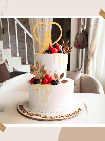 An elegant two-tier anniversary cake with a white chocolate drip, topped with fresh berries and a golden couple silhouette.
