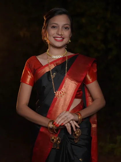 A direct and engaging portrait for Makar Sankrant. The subject looks straight at the camera with a warm smile, showcasing her traditional black saree and gold jewelry against a softly lit background.