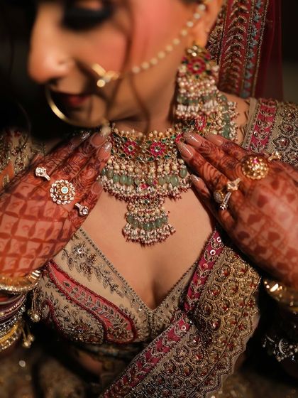 A close-up shot focusing on the bride's hands, adorned with henna and statement rings, as she adjusts her magnificent multi-colored kundan necklace.