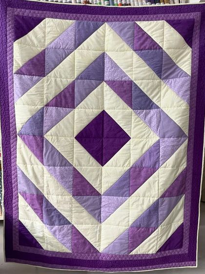 A quilt with a bold diamond pattern in shades of purple and cream.
