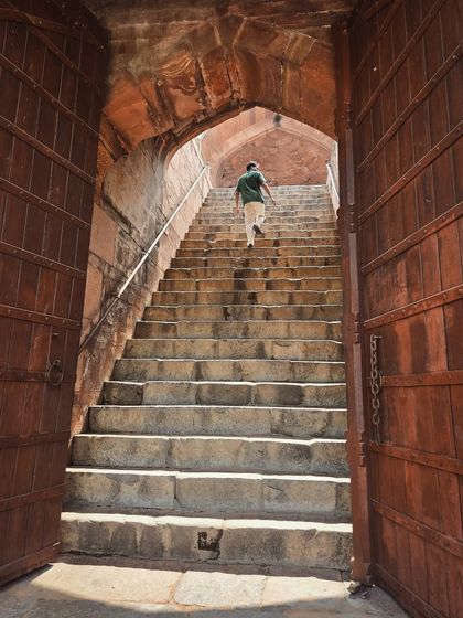 Looking up a grand stone staircase through massive wooden doors at a heritage site in Delhi.