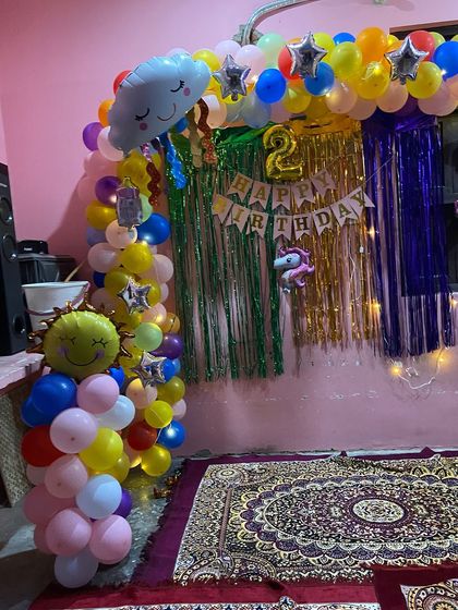 A cheerful and colorful home decoration for a second birthday. This theme includes a rainbow balloon arch with cute sun and cloud foil balloons.