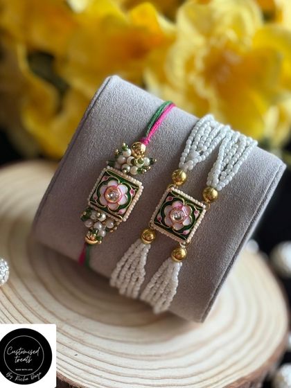 A delicate and pretty floral enamel Rakhi set. The soft pink and green colors with pearl tassels give this Bhaiya-Bhabhi set a fresh and modern feel.