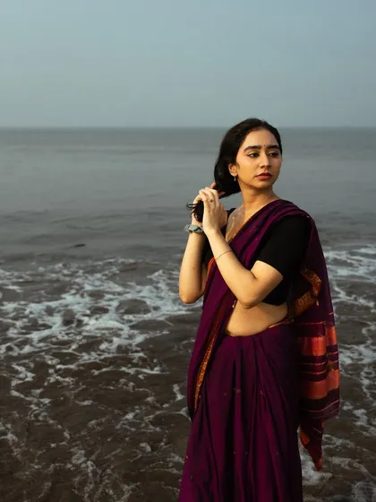 The movement of the saree in the water creates a beautiful, flowing texture in this beach portrait.