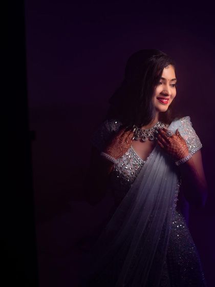 An artistic, low-light photo of Rakshita, where her smile and the sparkle of her outfit are the main focus.