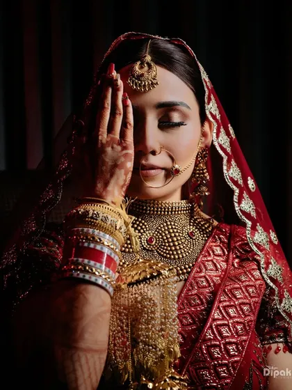 A stunning close-up of a bride, her eyes closed in a moment of quiet reflection before the ceremony. Her intricate jewelry and red veil are highlighted beautifully.