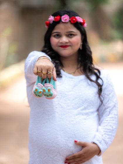 A sweet close-up of a mom-to-be holding a pair of tiny bunny shoes towards the camera.