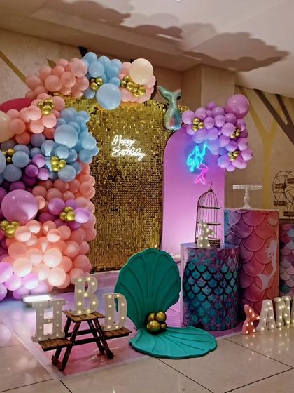 A side view of a mermaid-themed sixth birthday, showing the shimmering gold backdrop and pastel balloon arch.