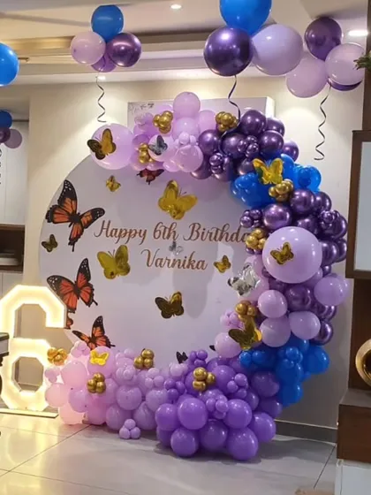 A beautiful butterfly theme for a 6th birthday. The circular backdrop is decorated with butterflies and a semi-arch of purple, pink, and blue balloons, complete with a light-up number '6'.