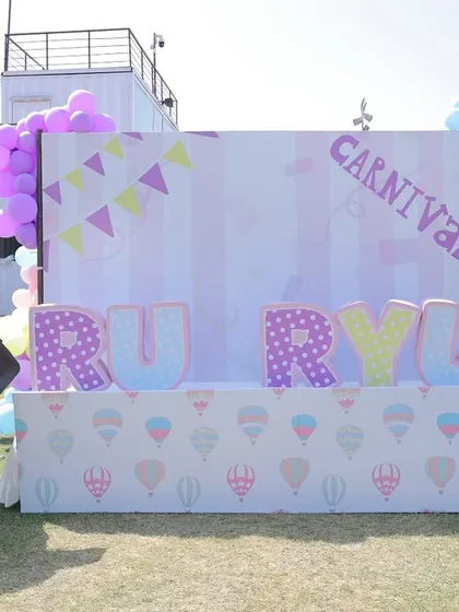 A custom backdrop for twins "Ru & Ryu" at their outdoor carnival party. The setup includes a life-sized elephant prop and large, decorated letters for a personalized touch.