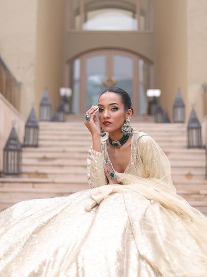 An elegant bride in an ivory lehenga. The makeup is classic, with a bold red lip and winged liner.