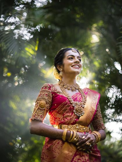 A joyful bride looking up, her face full of happiness. Her red saree and gold jewelry shine, creating a perfect bridal portrait.