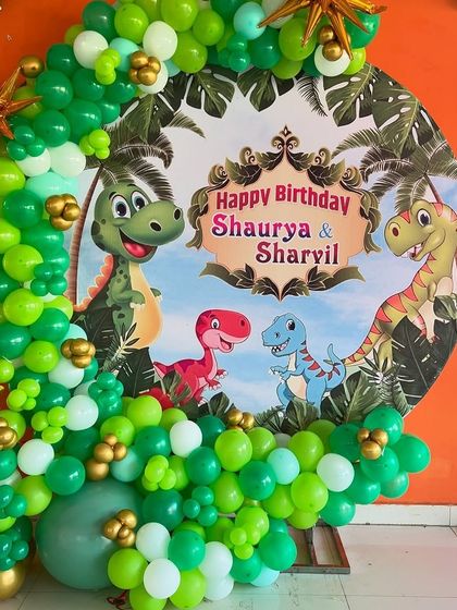 The organic balloon arch in shades of green, white, and gold perfectly frames the dinosaur-themed backdrop for this fun-filled kids' party.