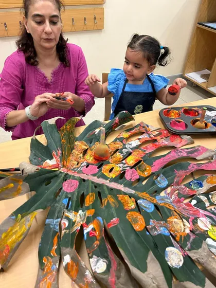 A large monstera leaf becomes a collaborative canvas for parents and children. This intergenerational art project allows for shared creativity, as different hands add layers of color and pattern, transforming a natural object into a collective masterpiece.